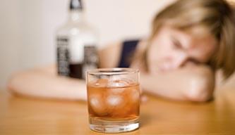 一个酗酒的女人拿着一瓶酒盯着一杯威士忌