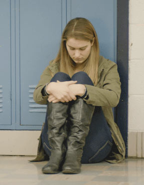 一个小女孩在学校走廊里抱着双腿。